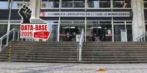 Fachada da Assembleia Legislativa de Minas Gerais (ALMG), com pessoas entrando e saindo do prédio. Na parte superior da escadaria, a placa institucional identifica o local. No canto superior esquerdo, o título “” e, à esquerda, o selo da campanha “Data-Base 2025: Eu não abro mão!”, com o desenho de um punho erguido sobre uma pilha de papéis.