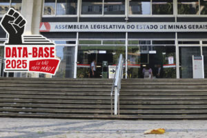 Fachada da Assembleia Legislativa de Minas Gerais (ALMG), com pessoas entrando e saindo do prédio. Na parte superior da escadaria, a placa institucional identifica o local. No canto superior esquerdo, o título “” e, à esquerda, o selo da campanha “Data-Base 2025: Eu não abro mão!”, com o desenho de um punho erguido sobre uma pilha de papéis.