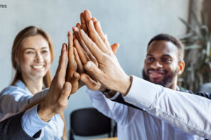 A imagem mostra quatro pessoas, dois e duas mulheres em um ambiente de trabalho com expressão dos rostos positiva e alegre, sugerindo uma celebração ou um momento de reconhecimento.