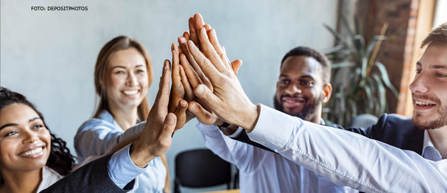 A imagem mostra quatro pessoas, dois e duas mulheres em um ambiente de trabalho com expressão dos rostos positiva e alegre, sugerindo uma celebração ou um momento de reconhecimento.