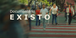 A imagem divulga o documentário “Existo”. Ao fundo, uma cena urbana com faixa de pedestres movimentada; várias pessoas aparecem desfocadas em movimento, enquanto duas mulheres com deficiência física, usando muletas, caminham com nitidez pelo centro da faixa. Sobre a imagem, os textos em destaque informam: “Documentário Existo”, data “24/4 (sexta-feira)”, horário “20h” e local “Una Cine Belas Artes”. À direita, destaca-se a mensagem “Inscrições abertas – vagas limitadas”. Na parte inferior, aparece o logotipo do SINJUS MG.
