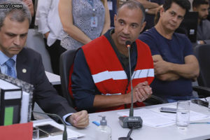 Wagner Ferreira, homem negro, grisalho, ele está vestido com um colete vermelho com faixas refletivas e fala ao microfone durante sessão da CPI da Lagoa da Pampulha. Conteúdo textual: OPINIÃO - JORNAL O TEMPO PUBLICA ARTIGO DE WAGNER FERREIRA SOBRE LAGOA DA PAMPULHA.