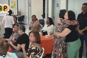 rupo de aposentados e pensionistas reunidos com Alex Aguiar, diretor de aposentados e pensionistas do SINJUS-MG, em reunião de reencontro do NAP (Núcleo de Aposentados e Pensionistas). As expressões faciais demonstram que o grupo está alegre e descontraído.