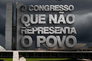 Imagem Acessível: A imagem mostra o prédio do Congresso Nacional em Brasília sob um céu nublado e escuro, com urubus voando e pousados no gramado em primeiro plano, transmitindo um clima de crítica e pessimismo. Em destaque, grandes letras de concreto rachadas trazem a frase: “O CONGRESSO QUE NÃO REPRESENTA O POVO”. Logo abaixo, sobre uma faixa branca e vermelha, repete-se a mensagem: “O Congresso que não representa o povo”. No canto superior esquerdo está escrito “PEC da Impunidade”, e no canto superior direito aparece o crédito da imagem “Fenajud”.