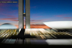 Imagem noturna do Congresso Nacional (duas torres centrais entre duas cúpulas, uma virada para baixo e outra virada para cima).