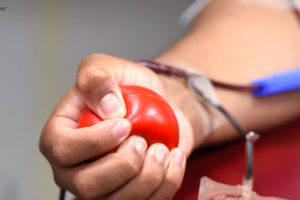 Foto de mulher de pele negra apertando uma pequena bola vermelha enquanto doa sangue.