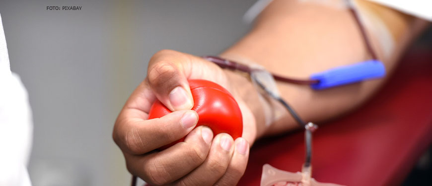 Foto de mulher de pele negra apertando uma pequena bola vermelha enquanto doa sangue.
