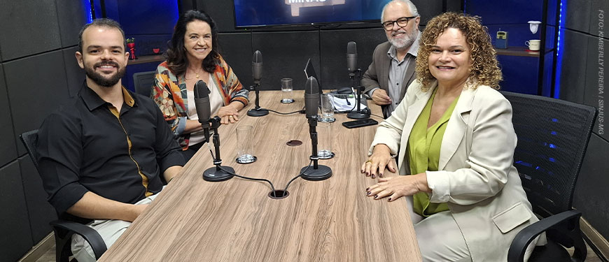 Imagem Acessível: Na mesa de um estúdio de gravação, há quatro pessoas sentadas: do lado esquerdo estão o coordenador-geral do SINJUS-MG, Felipe Rodrigues e a presidente da Associação Nacional dos Auditores Fiscais de Tributos Estaduais (Febrafite), Maria Aparecida Meloni (Papá), à direita estão Rose Laura Lopes Pinto, diretora da Associação dos Funcionários Fiscais de Minas Gerais (Affemg) e do Sindifisco-MG junto do anfitrião, o jornalista Orion Teixeira. Sobre a mesa há microfones, copos, papéis, um celular e um notebook. Ao fundo, uma televisão exibe o logotipo do podcast “Se Liga, Minas”, com o desenho do mapa de Minas Gerais e um ícone de podcast. Conteúdo textual: PODCAST - SINJUS debate educação fiscal em novo episódio do "Se Liga, Minas"