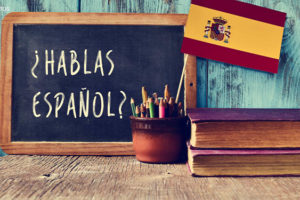 Imagem acessível: Imagem com livros, lápis de cor e quadro negro com os dizeres "¿Hablas español?"
