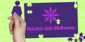 l: sobre um fundo verde pastel há um quebra cabeças lilás prestes a ser finalizado. Na parte central que está montada, há o logo do Núcleo das Mulheres do SINJUS. Uma das peças que será encaixada tem a silhueta feminina e está nas mãos de uma mulher, remetendo à ideia de participação e construção coletiva.