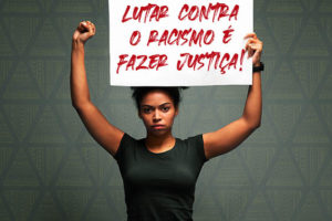 fundo cinza com destaque ao centro para um jovem negra, de cabelos crespos, usando camisa preta e segurando ao alto um cartaz com os dizeres: Lutar contra o racismo é fazer Justiça!