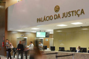 Fotografia da parte interna do Palácio da Justiça, na foto se ve um balcão de pedra com computadores em cima, e pessoas trabalhando, também na imagem se um ambiente de movimentação com pessoas andando.