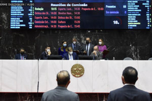 Deputados em votação no Plenário da ALMG, em destaque está a mesa diretiva da sessão com o painel luminoso ao fundo.