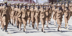 Policiais militares, homens e mulheres, estão vestidos com farda marrom e marcham enfileirados. Conteúdo textial: IGUALDADE - Justiça reconhece direito de candidata injustiçada no concurso da PMMG retornar ao concurso.