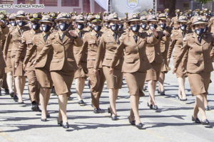 Policiais militares, homens e mulheres, estão vestidos com farda marrom e marcham enfileirados. Conteúdo textial: IGUALDADE - Justiça reconhece direito de candidata injustiçada no concurso da PMMG retornar ao concurso.