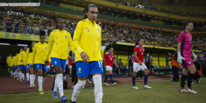 Seleção brasileira feminina de futebol entrando em campo, elas estão vestidas com o uniforme verde amarelo da CBF. Em destaque está a jogadora Marta. Conteúdo textual: COPA DO MUNDO FEMININA - SINJUS REQUER QUE TJ FLEXIBILIZE EXPEDIENTE NOS DIAS DE JOGOS.