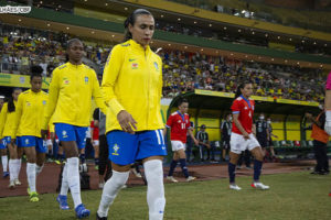 Seleção brasileira feminina de futebol entrando em campo, elas estão vestidas com o uniforme verde amarelo da CBF. Em destaque está a jogadora Marta. Conteúdo textual: COPA DO MUNDO FEMININA - SINJUS REQUER QUE TJ FLEXIBILIZE EXPEDIENTE NOS DIAS DE JOGOS.