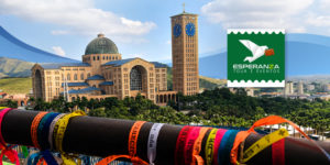 Imagem acessível: A imagem divulga a viagem para Aparecida do Norte, que ocorrerá entre os dias 23 a 26 de novembro, com a proposta de proporcionar momentos de fé e reflexão. Ao fundo, aparece o Santuário Nacional de Nossa Senhora Aparecida, visto a partir da passarela decorada com fitas coloridas. A peça destaca que as vagas são limitadas e orienta a inscrição pelo formulário.