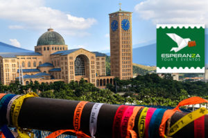 Imagem acessível: A imagem divulga a viagem para Aparecida do Norte, que ocorrerá entre os dias 23 a 26 de novembro, com a proposta de proporcionar momentos de fé e reflexão. Ao fundo, aparece o Santuário Nacional de Nossa Senhora Aparecida, visto a partir da passarela decorada com fitas coloridas. A peça destaca que as vagas são limitadas e orienta a inscrição pelo formulário.
