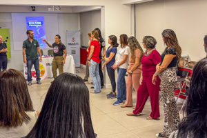 A imagem mostra um grupo de mulheres reunido durante uma atividade prática de defesa pessoal. Em destaque, o título diz “Workshop do NM ensina como identificar situações de risco e agir com segurança”. As participantes acompanham as orientações da instrutores durante a ação promovida pelo Núcleo das Mulheres (NM) do SINJUS-MG.