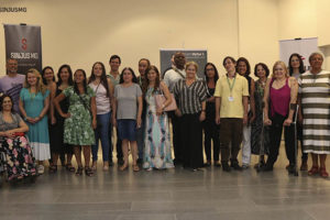 Fotografia com diversas pessoas, com e sem deficiência: são participantes e palestrantes do evento do núcleo da pessoa com deficiência do SINJUS e diretores do sindicato. O grupo está em um ambiente amplo, de paredes em tom creme e chão acinzentado; atrás das pessoas, há alguns banners.