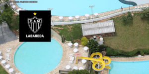 Vista aérea da sede do Clube Labareda com enquadramento no complexo de piscinas. No canto superior esquerdo, há sobreposição de uma imagem com o escudo do Clube Atlético Mineiro.