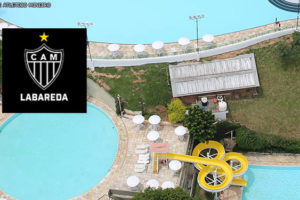 Vista aérea da sede do Clube Labareda com enquadramento no complexo de piscinas. No canto superior esquerdo, há sobreposição de uma imagem com o escudo do Clube Atlético Mineiro.