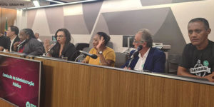 Fotografia de uma sala de audiência da ALMG com um palanque onde se vê pessoas sentadas atrás do mesmo, entre elas o diretor do SINJUS Jonas Araújo.