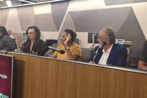 Fotografia de uma sala de audiência da ALMG com um palanque onde se vê pessoas sentadas atrás do mesmo, entre elas o diretor do SINJUS Jonas Araújo.