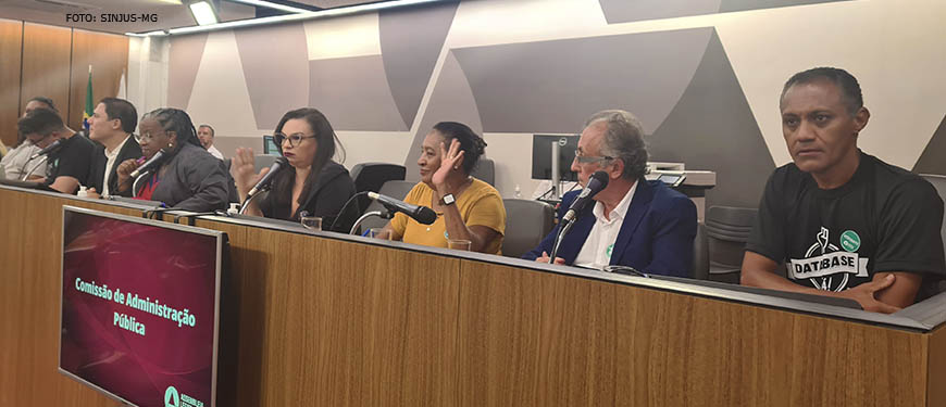 Fotografia de uma sala de audiência da ALMG com um palanque onde se vê pessoas sentadas atrás do mesmo, entre elas o diretor do SINJUS Jonas Araújo.