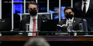 Presidente do Senado Federal, Rodrigo Pacheco (DEM-MG), homem de pele clara e olhos e cabelos castanhos, e o secretário-geral da Mesa do Senado Federal, Gustavo A. Sabóia Vieira, homem de pele clara e cabelo preto. Ambos estão com máscaras e ternos pretos, camisas brancas e gravatas vermelhas.