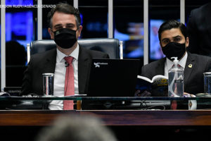 Presidente do Senado Federal, Rodrigo Pacheco (DEM-MG), homem de pele clara e olhos e cabelos castanhos, e o secretário-geral da Mesa do Senado Federal, Gustavo A. Sabóia Vieira, homem de pele clara e cabelo preto. Ambos estão com máscaras e ternos pretos, camisas brancas e gravatas vermelhas.
