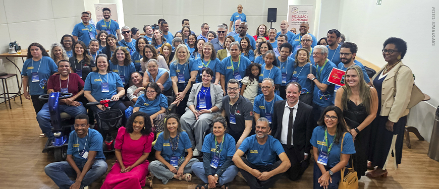 A imagem retrata um grande grupo de servidores que participaram do seminário, reunidos em uma sala, muitos deles vestindo camisetas azuis com a logo da identidade do evento, em pose para a foto em uma demonstração de diversidade e inclusão. O texto em destaque ressalta que o encontro reuniu pessoas com deficiência que enfrentam barreiras físicas e atitudinais no TJMG e no MPMG.