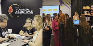 A arte mostra ao fundo registros de algumas tecnologias sendo apresentadas na Mostra de Tecnologias Assistivas e Soluções de Acessibilidade no TJMG. A montagem reúne fotos de visitantes conhecendo e experimentando diferentes recursos de tecnologia assistiva durante a exposição promovida pelo SINJUS-MG, com demonstrações e interação entre participantes e expositores.
