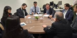 Imagem Acessível: Reunião em uma sala com pessoas sentadas ao redor de uma mesa redonda, estão presentes representantes do Serjusmig, Sindojus/MG, o presidente do TJMMG, Jadir Silva, o procurador do Estado, Daniel Cabalero Saldanha, o desembargador do TJMG, Paulo Mendes Álvares e o diretor de assuntos Jurídicos do SINJUS-MG, Felipe Rodrigues, que está assinando um documento. Conteúdo textual: Conquista - Servidores do TJM vão receber juros e correção das Datas-Bases de 2014 a 2017.