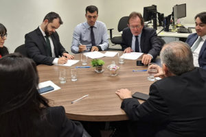 Imagem Acessível: Reunião em uma sala com pessoas sentadas ao redor de uma mesa redonda, estão presentes representantes do Serjusmig, Sindojus/MG, o presidente do TJMMG, Jadir Silva, o procurador do Estado, Daniel Cabalero Saldanha, o desembargador do TJMG, Paulo Mendes Álvares e o diretor de assuntos Jurídicos do SINJUS-MG, Felipe Rodrigues, que está assinando um documento. Conteúdo textual: Conquista - Servidores do TJM vão receber juros e correção das Datas-Bases de 2014 a 2017.
