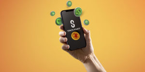 Mão segura um celular com a tela exibindo o logotipo do Sinjusnet, informativo do SINJUS-MG. Ao redor do aparelho, flutuam ícones 3D do WhatsApp, de notificações e mensagens, sobre um fundo em degradê laranja.