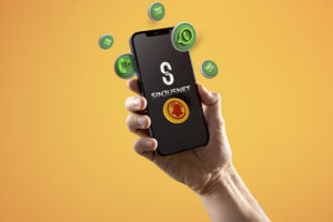 Mão segura um celular com a tela exibindo o logotipo do Sinjusnet, informativo do SINJUS-MG. Ao redor do aparelho, flutuam ícones 3D do WhatsApp, de notificações e mensagens, sobre um fundo em degradê laranja.