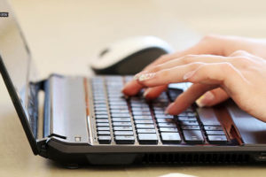 Enquadramento fechado que mostra apenas as mãos de uma pessoa digitando em um teclado de notebook.