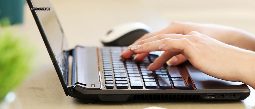 Enquadramento fechado que mostra apenas as mãos de uma pessoa digitando em um teclado de notebook.
