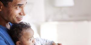 Imagem acessível: A imagem informa sobre condições de trabalho. À esquerda, um homem segura um bebê no colo em ambiente doméstico, demonstrando cuidado e vínculo familiar. No topo, aparece o título “Condições de trabalho”. À direita, em destaque, o texto informa: “Servidores terão teletrabalho integral por seis meses após o fim da licença-paternidade”, com trechos em destaque em amarelo e branco sobre fundo clato. Na parte inferior, está o logotipo do SINJUS MG.