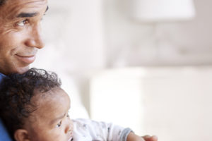 Imagem acessível: A imagem informa sobre condições de trabalho. À esquerda, um homem segura um bebê no colo em ambiente doméstico, demonstrando cuidado e vínculo familiar. No topo, aparece o título “Condições de trabalho”. À direita, em destaque, o texto informa: “Servidores terão teletrabalho integral por seis meses após o fim da licença-paternidade”, com trechos em destaque em amarelo e branco sobre fundo clato. Na parte inferior, está o logotipo do SINJUS MG.