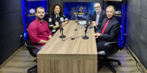 Imagem Acessível: Quatro pessoas estão sentadas em uma mesa de estúdio de gravação, com microfones à frente, participando da gravação de um videocast. Os participantes são: a ministra do TSE, Edilene Lobo, representando da Affemg, o jornalista Marco Túlio da Silva, o diretor de Assuntos Jurídicos do SINJUS-MG, Felipe Rodrigues e Orion Teixeira, jornalista e anfitrião.Atrás dos participantes, há uma TV com o logotipo do programa “Se Liga, Minas”. Conteúdo textual: VIDEOCAST - Novo episódio do Se Liga, Minas discute os desafios da democracia na era digital.