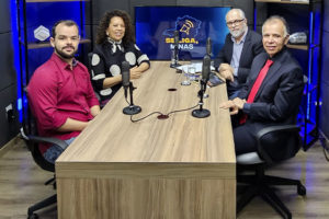 Imagem Acessível: Quatro pessoas estão sentadas em uma mesa de estúdio de gravação, com microfones à frente, participando da gravação de um videocast. Os participantes são: a ministra do TSE, Edilene Lobo, representando da Affemg, o jornalista Marco Túlio da Silva, o diretor de Assuntos Jurídicos do SINJUS-MG, Felipe Rodrigues e Orion Teixeira, jornalista e anfitrião.Atrás dos participantes, há uma TV com o logotipo do programa “Se Liga, Minas”. Conteúdo textual: VIDEOCAST - Novo episódio do Se Liga, Minas discute os desafios da democracia na era digital.