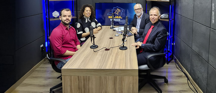 Imagem Acessível: Quatro pessoas estão sentadas em uma mesa de estúdio de gravação, com microfones à frente, participando da gravação de um videocast. Os participantes são: a ministra do TSE, Edilene Lobo, representando da Affemg, o jornalista Marco Túlio da Silva, o diretor de Assuntos Jurídicos do SINJUS-MG, Felipe Rodrigues e Orion Teixeira, jornalista e anfitrião.Atrás dos participantes, há uma TV com o logotipo do programa “Se Liga, Minas”. Conteúdo textual: VIDEOCAST - Novo episódio do Se Liga, Minas discute os desafios da democracia na era digital.