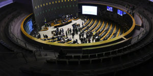 oto mostra o plenário da Câmara dos Deputados, vista do alto, com parlamentares em pé e sentados, durante uma sessão.