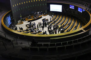 oto mostra o plenário da Câmara dos Deputados, vista do alto, com parlamentares em pé e sentados, durante uma sessão.