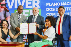 Presidente da República, Luiz Inácio Lula da Silva e Ministro dos Direitos Humanos e da Cidadania do Brasil, Silvio Almeida em cerimônia de lançamento do Novo Viver Sem Limite, no Palácio do Planalto. Eles estão cumprimentando pessoas com deficiência e exibem documento assinado na ocasião.