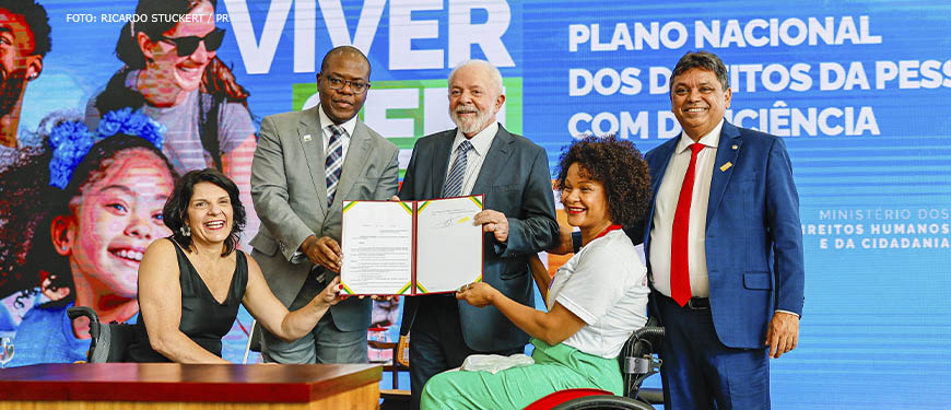 Presidente da República, Luiz Inácio Lula da Silva e Ministro dos Direitos Humanos e da Cidadania do Brasil, Silvio Almeida em cerimônia de lançamento do Novo Viver Sem Limite, no Palácio do Planalto. Eles estão cumprimentando pessoas com deficiência e exibem documento assinado na ocasião.