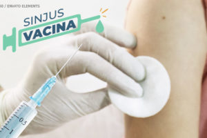 Imagem ampliada de uma mão com luvas de látex segurando uma seringa, que está prestes a ser aplicada em um braço feminino. No topo há o logo da iniciativa "SINJUS VACINA".